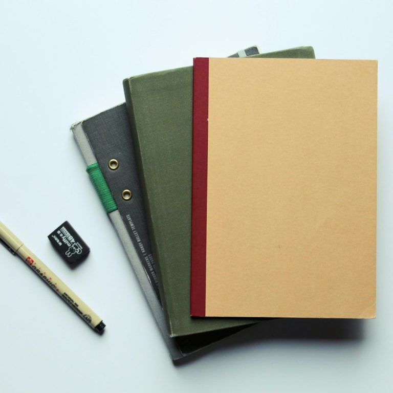 Eine Stapel Bücher in verschiedenen Farben, daneben ein Bleistift und ein Radiergummi.
