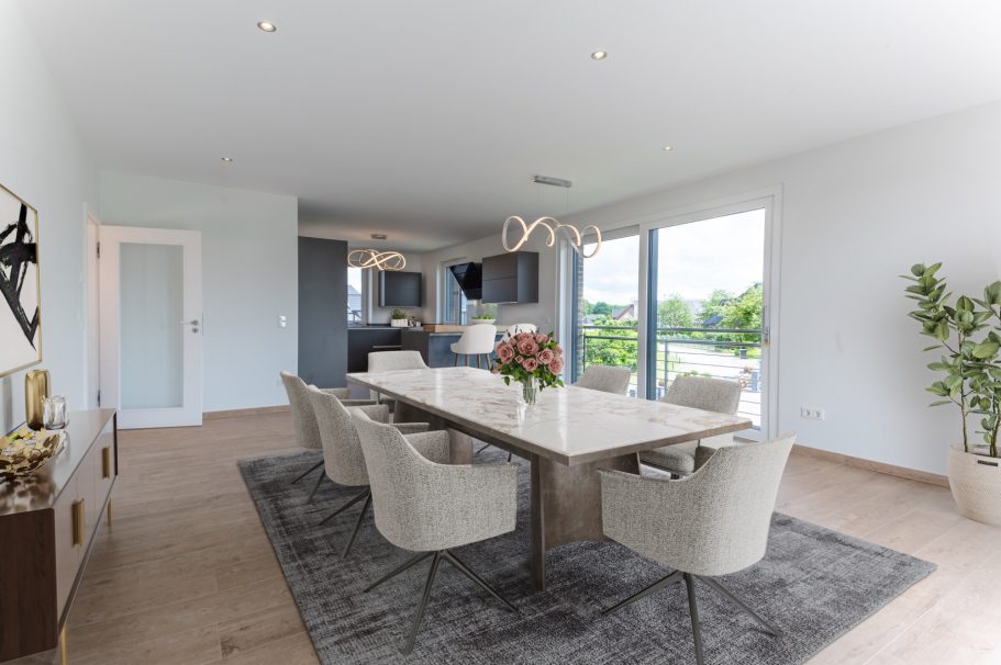 Moderne Esszimmer mit Tisch, Stühlen und großen Fenstern, die Licht hereinlassen.