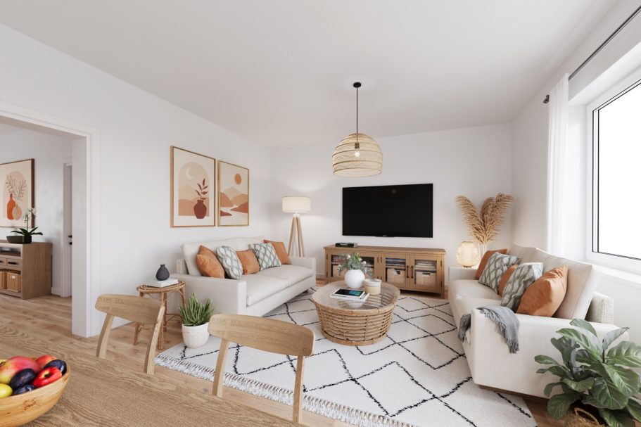 Helles Wohnzimmer mit beigem Sofa, TV, Pflanzen und einem runden Tisch auf einem gemusterten Teppich.