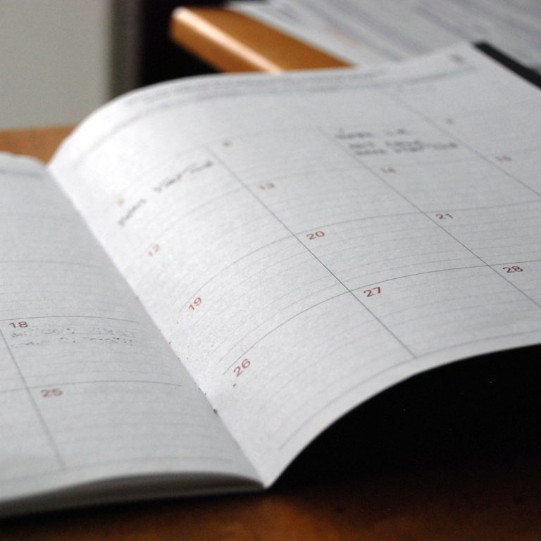 Ein geöffneter Kalender mit hervorgehobenen Terminen auf einer Tischoberfläche.