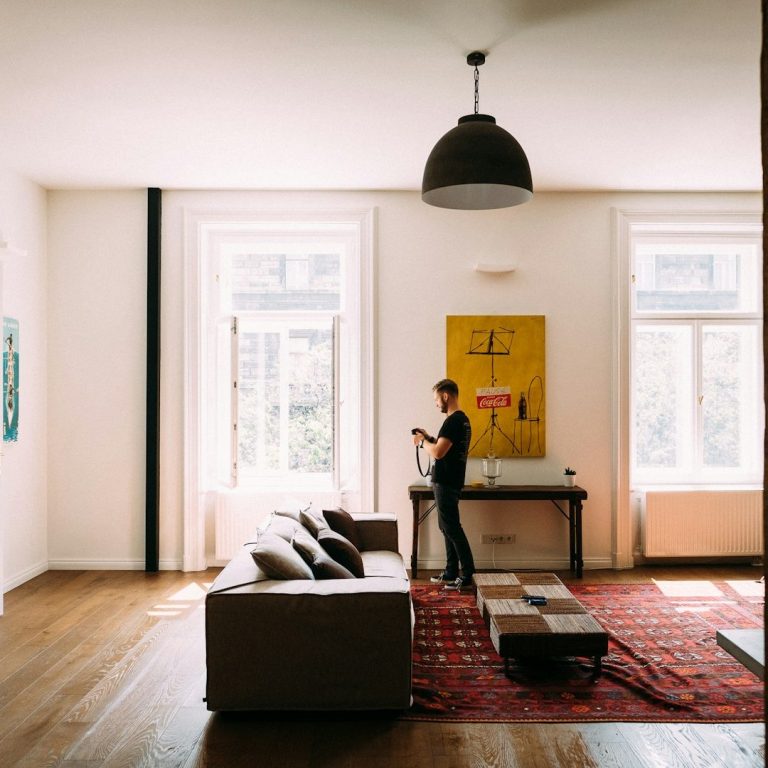 Moderne Wohnung mit hellem Raum, Sofas, Fenstern und einem Mann mit Smartphone.