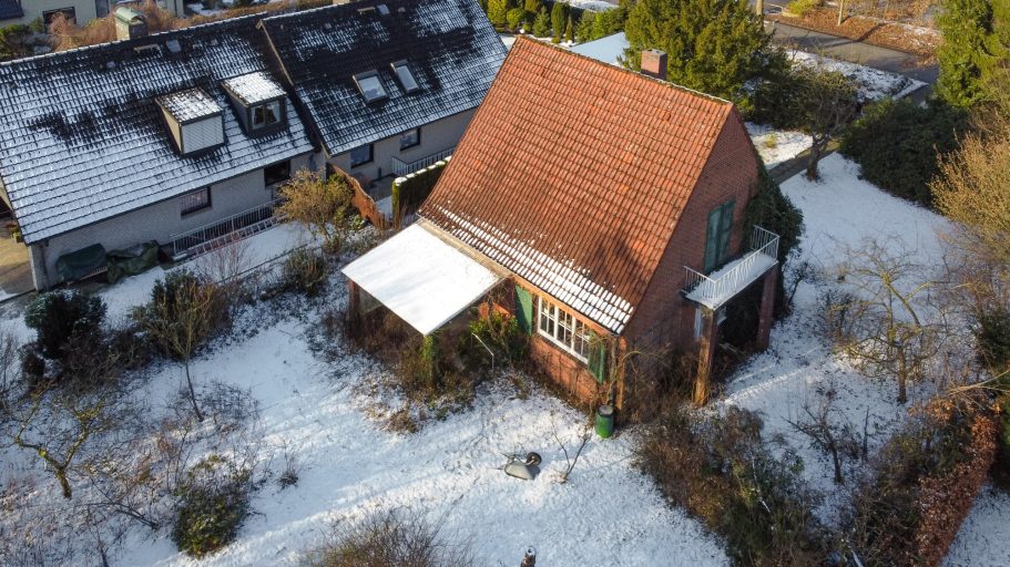 Einfamilienhaus mit rotem Dach und schneebedecktem Garten, umgeben von Bäumen.