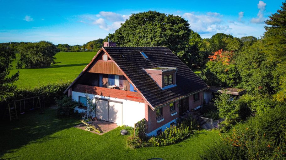 Ein großes, modernes Haus umgeben von Grünflächen und Bäumen unter blauem Himmel.