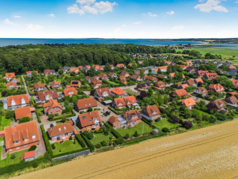 Luftaufnahme eines Wohngebiets mit roten Dächern und viel grünem Raum am Strand.