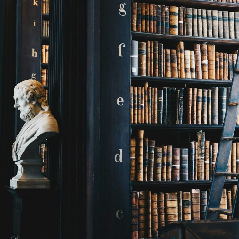 Büste eines Mannes vor einem Bücherregal mit zahlreichen alten Büchern.