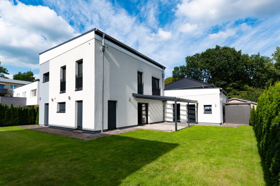 Modernes, zweistöckiges weißes Haus mit Garten und Garage, umgeben von Bäumen.